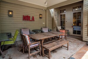 Une terrasse extérieure avec une table et des chaises en bois, une chaise verte et un mur sur lequel on peut voir le mot « NOLA ».