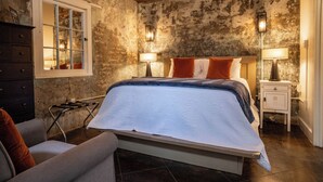 A bedroom with a bed, bedside lamps, a window, a dresser, and a chair. - Engine 24 Firehouse Courtyard Room 5 (New Orleans)