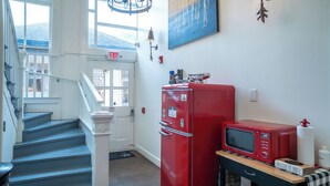Un pasillo con un refrigerador rojo, un microondas y una mesita con un letrero.