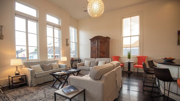 A spacious living room with a large window, a wooden cabinet, and a dining area with a red chair. - Engine 24 Firehouse Penthouse Suite (New Orleans)