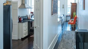 A spacious kitchen with a central island, a dining area with a red chair, and a hallway leading to a living room. - Engine 24 Firehouse Penthouse Suite (New Orleans)