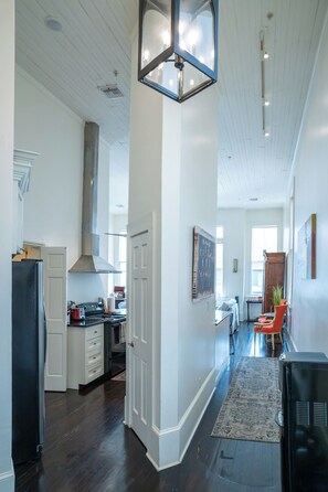 A spacious kitchen with a central island, a dining area with a red chair, and a hallway leading to a living room.