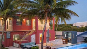 Una casa de dos pisos con fachada roja, piscina y palmeras.