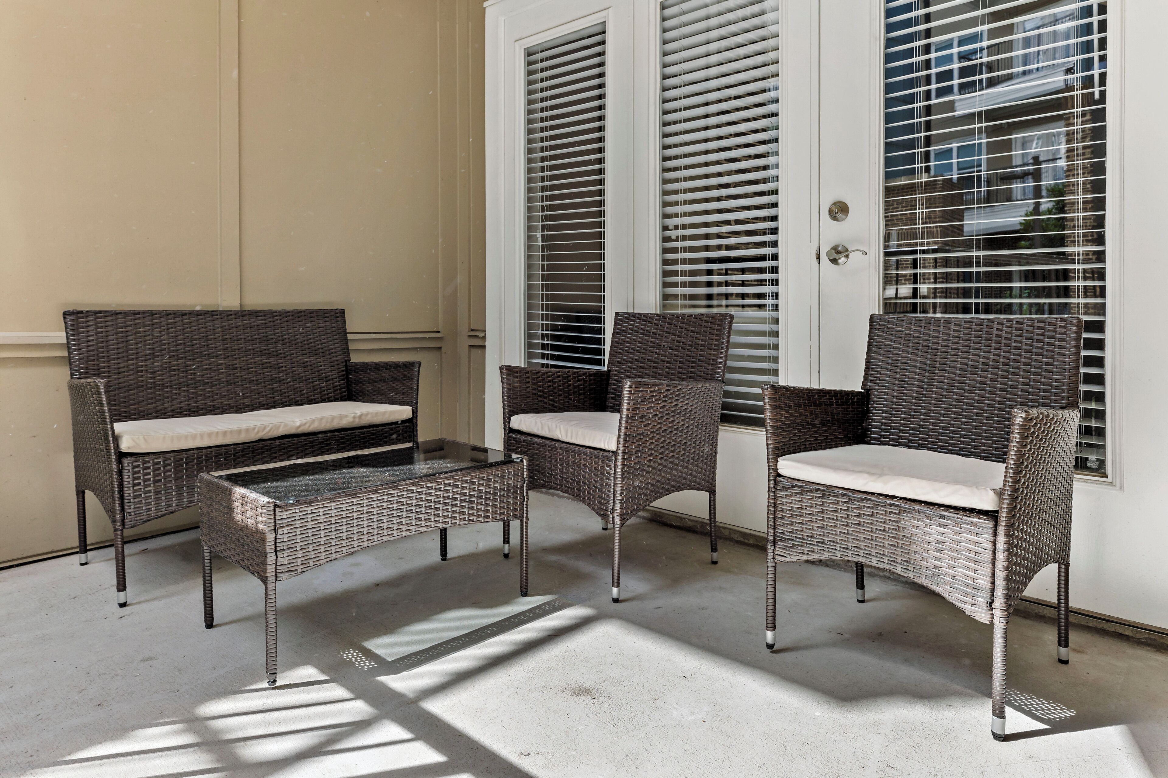 A patio area with wicker furniture, including a sofa and two chairs, near a white door with blinds.