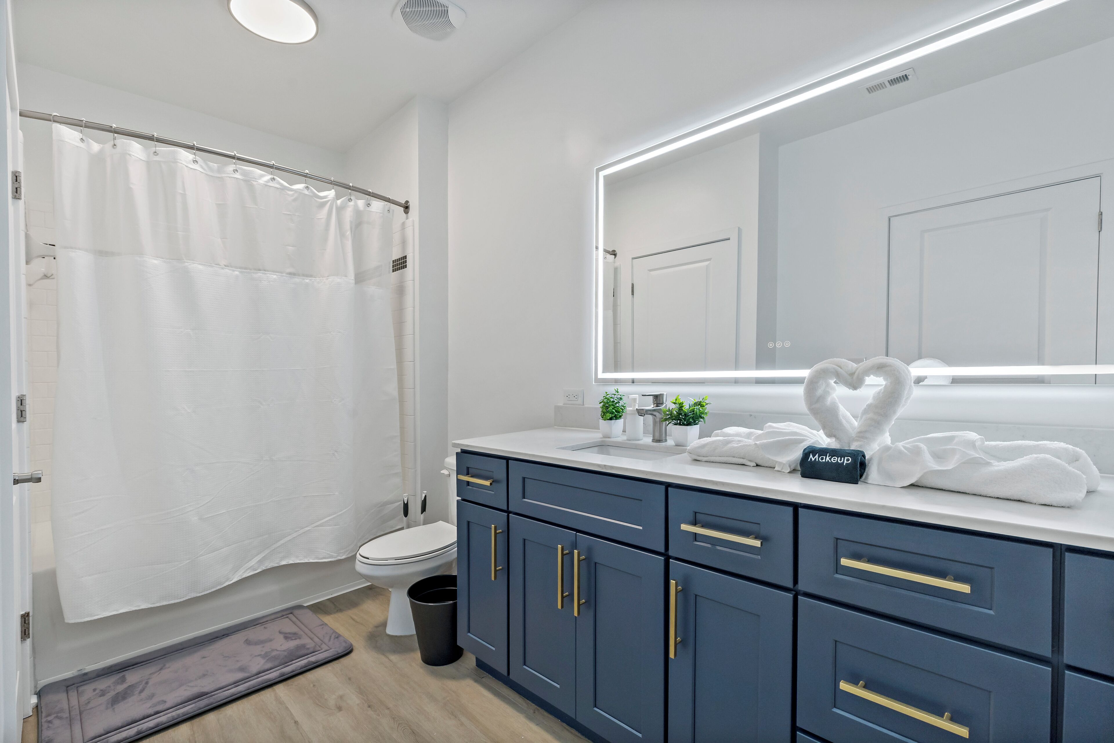 Een moderne badkamer met een witte douchegordijn, een toilet, een wastafel met spiegel, en een badkamermeubel met lades.