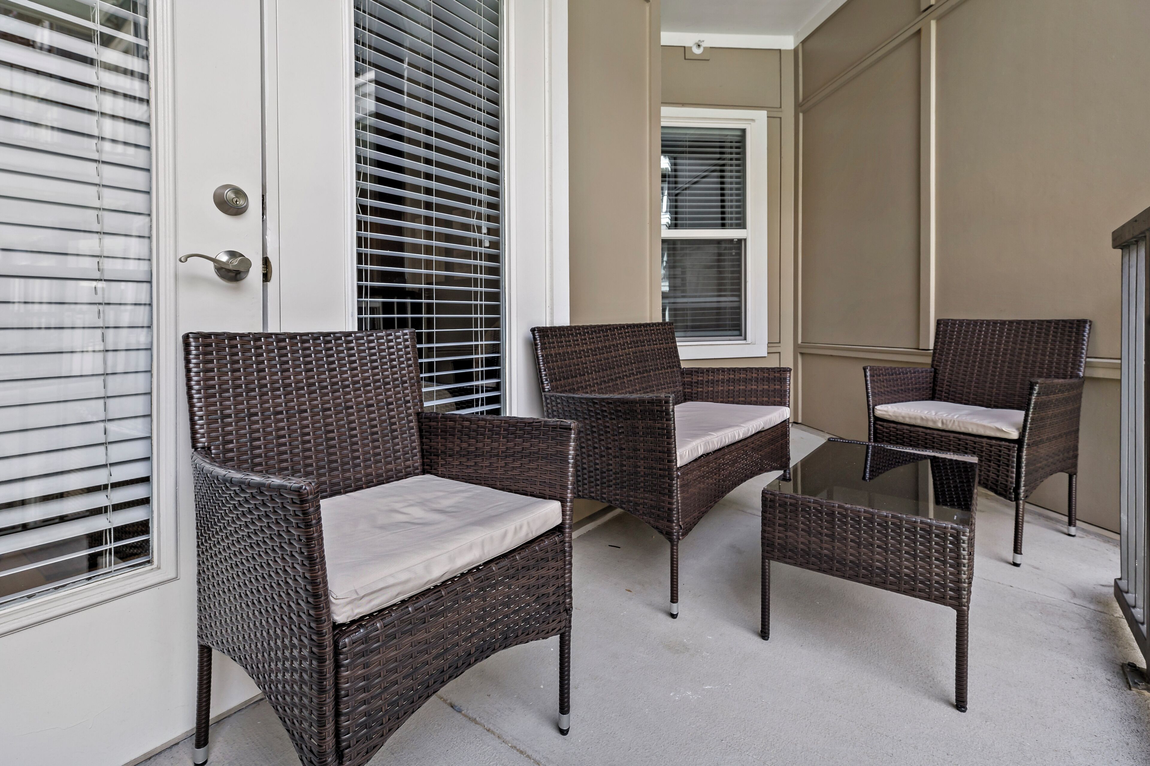 A patio area with wicker furniture, including chairs and a bench, near a door with a window.