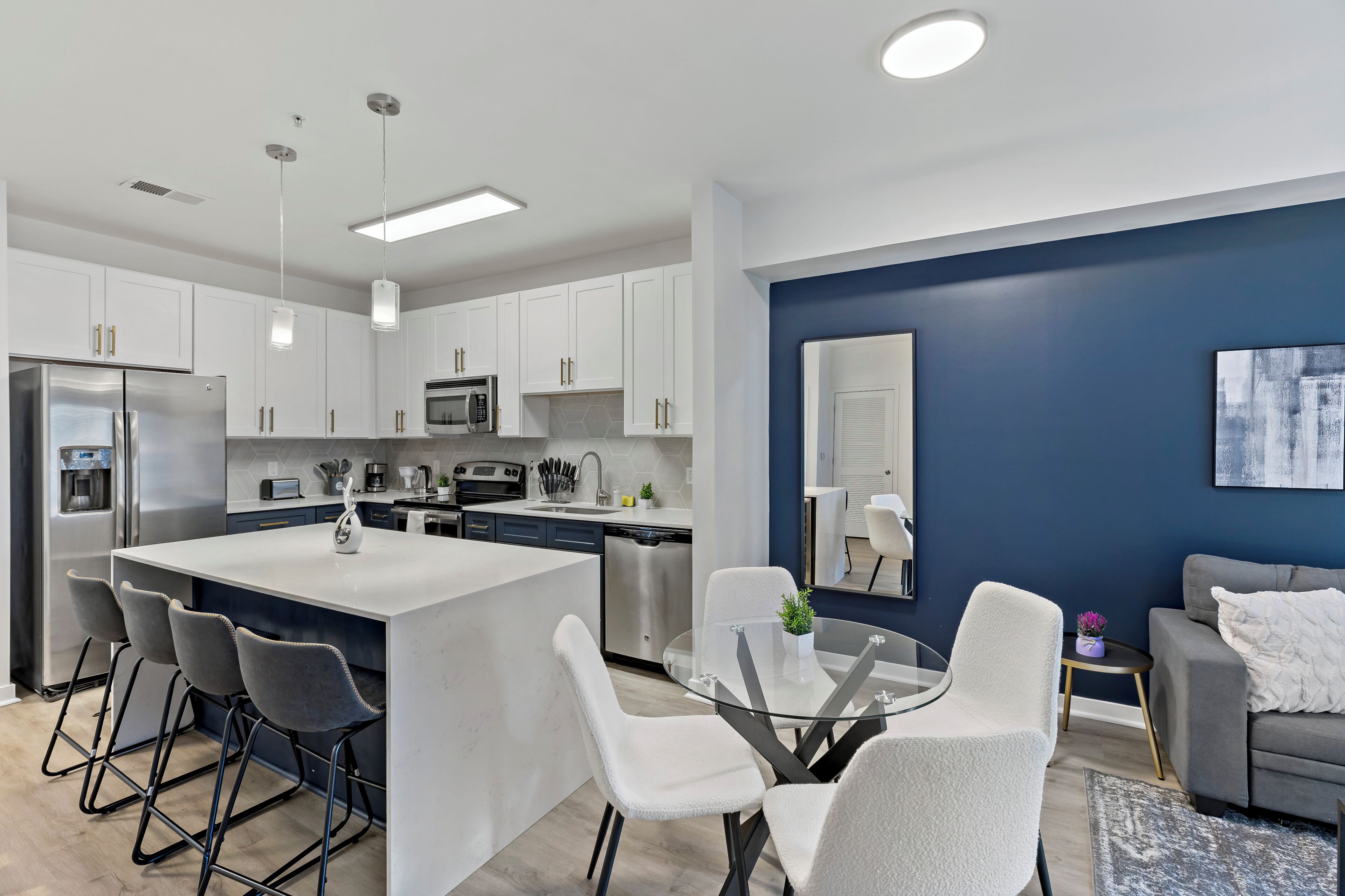Una cocina moderna con armarios blancos, un refrigerador de acero inoxidable y una isla central con taburetes de bar.