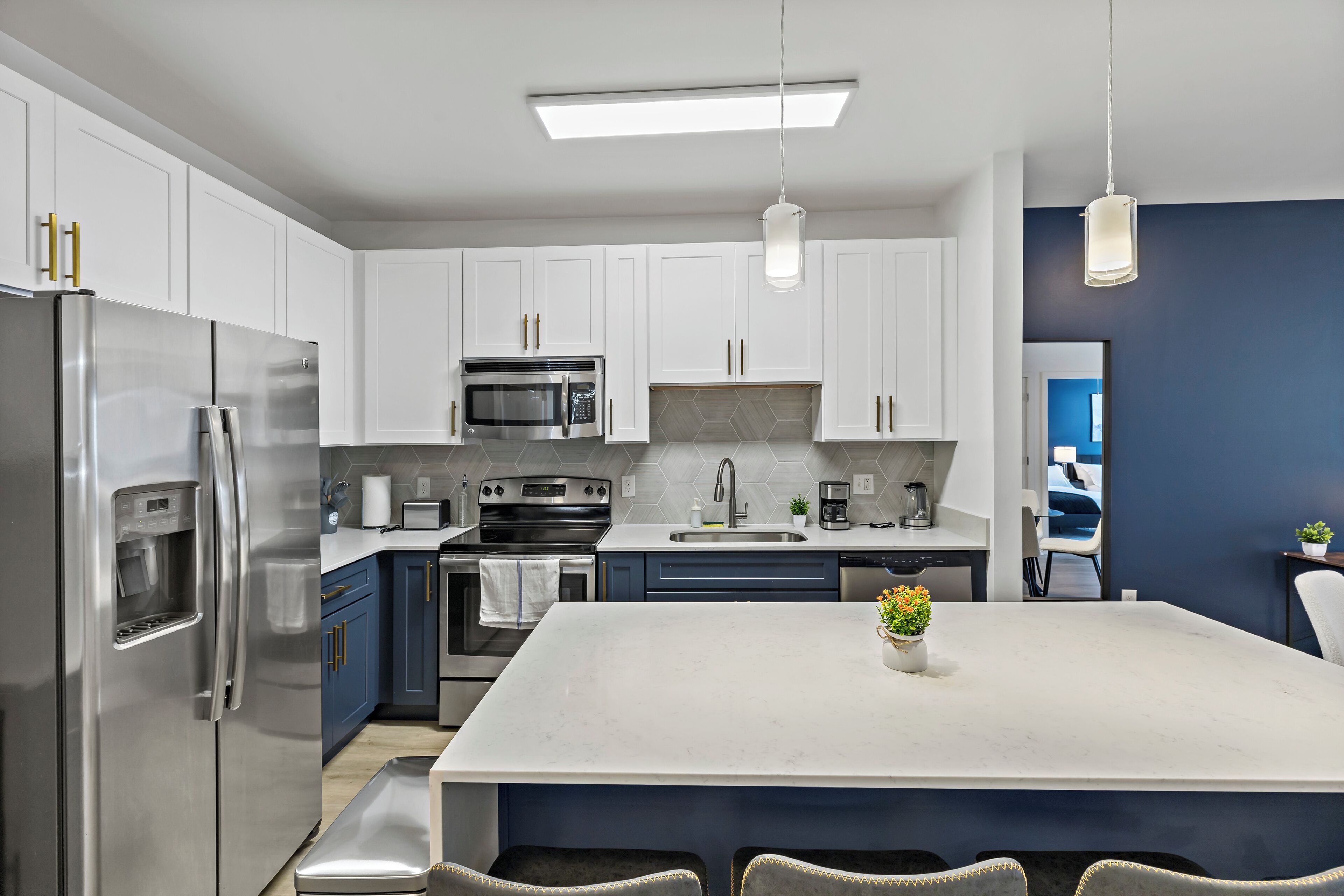 A modern kitchen with white cabinets, stainless steel appliances, a central island, and a hanging pendant light.
