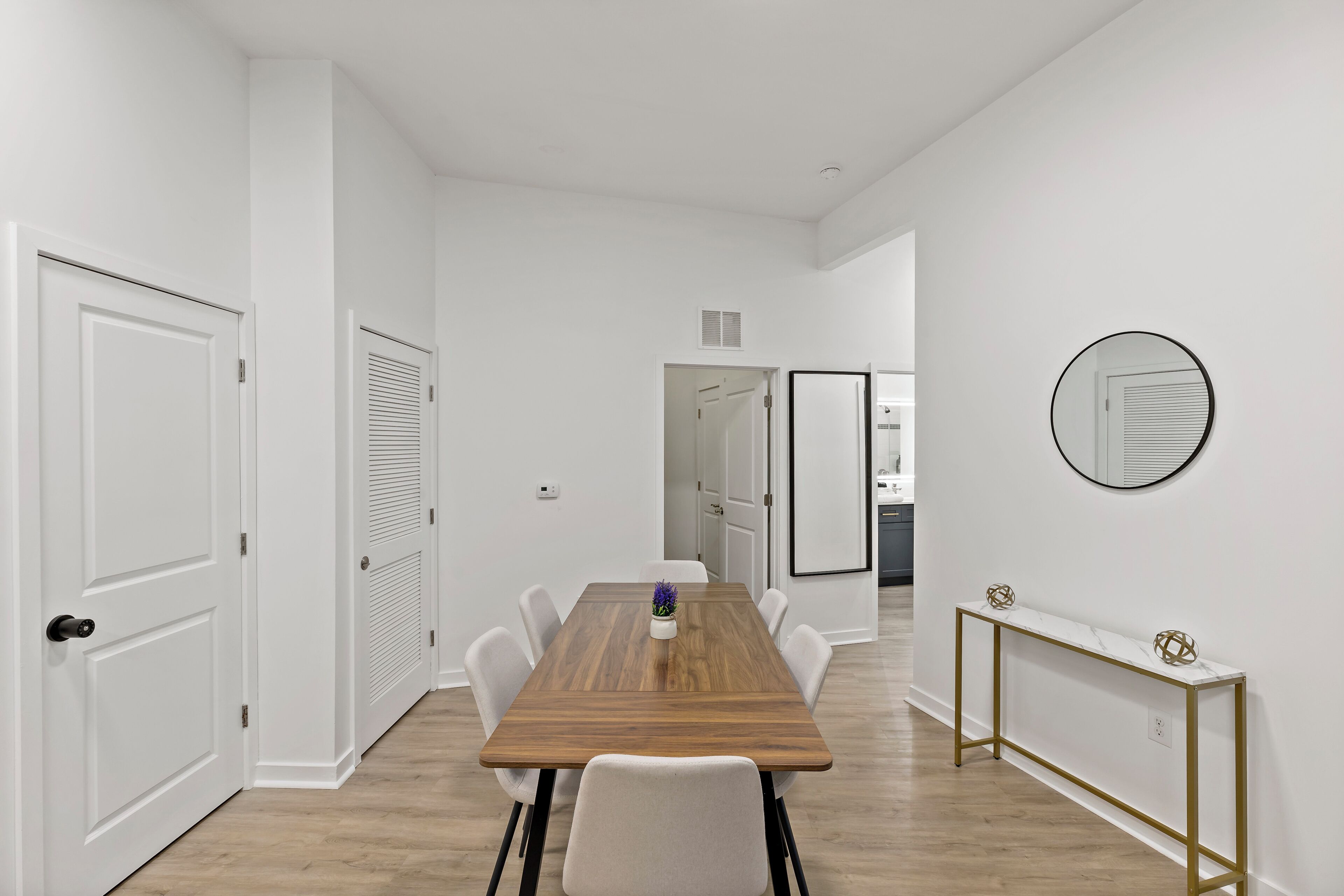 Un espace repas moderne avec une table en bois, des chaises blanches et une console dorée.