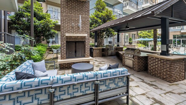 Eine Terrasse mit Kamin aus Ziegelsteinen, Sitzgelegenheiten im Freien und einem überdachten Grillbereich.