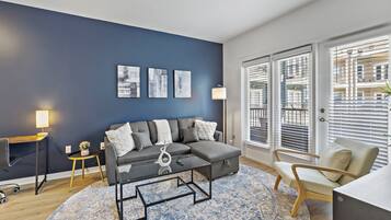 A modern living room with a sectional sofa, a glass coffee table, a round rug, and a desk with a lamp.