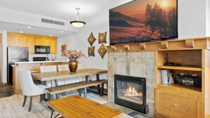 A modern living room with a fireplace, a dining area, and a kitchen in the background.