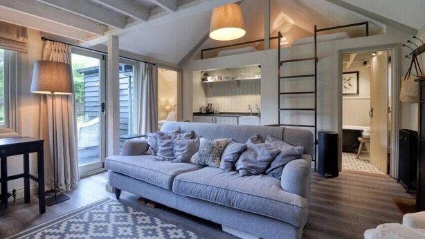 Un salon moderne avec un canapé gris, un tapis à motifs et un plafond avec des poutres apparentes.