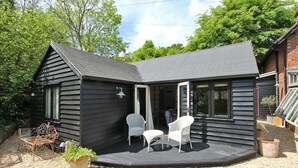 Une petite cabane noire dotée d’une terrasse, de chaises blanches et d’un banc.
