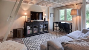Une chambre avec un plafond en pente, un lit, un bureau, une chaise, un téléviseur et une fenêtre avec des rideaux.