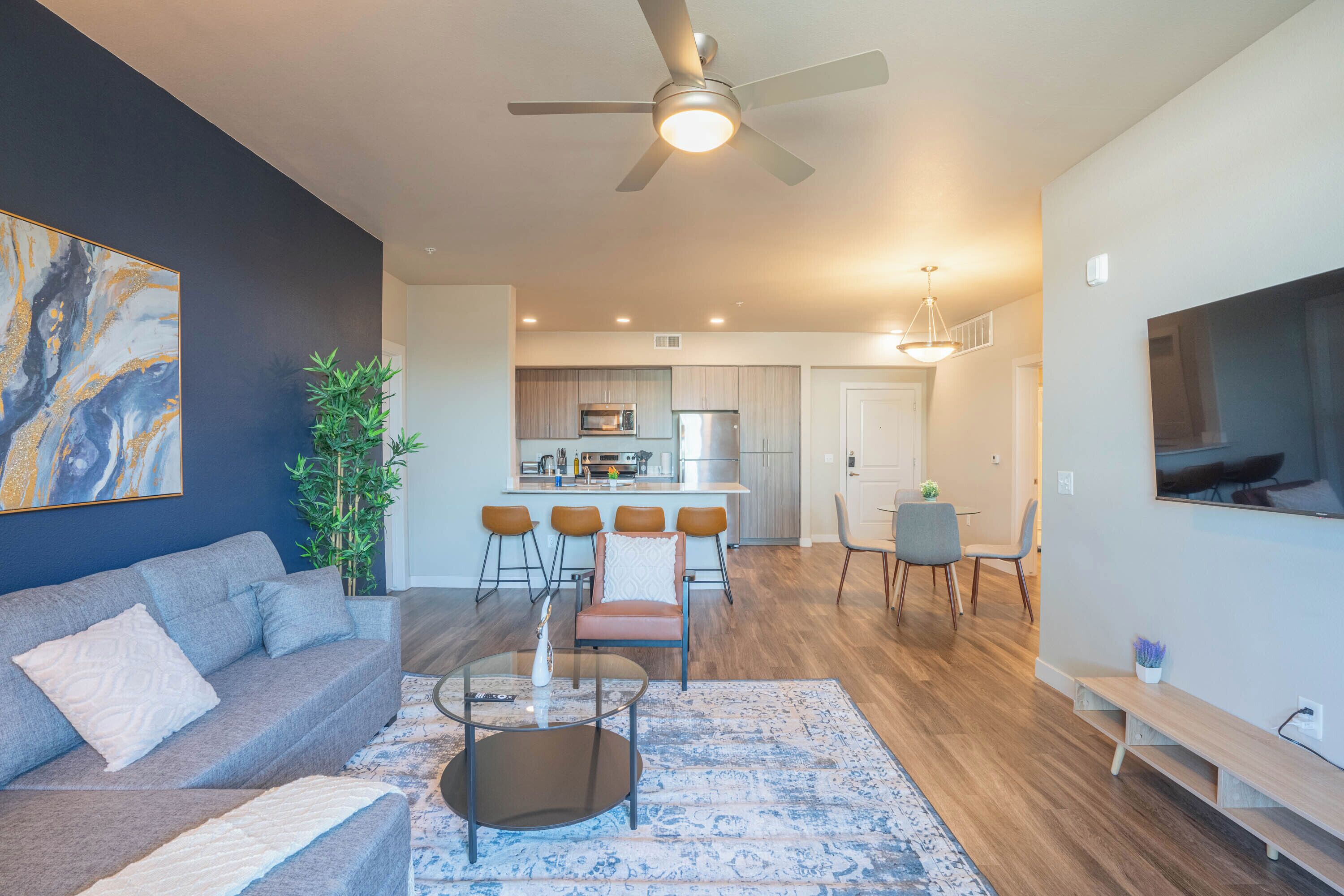 A modern living room with a grey sofa, a coffee table, and a dining area with bar stools.