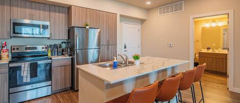 A modern kitchen with stainless steel appliances, wooden cabinets, and a central island with bar stools.