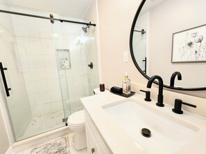 A modern bathroom with a glass-enclosed shower, a white sink with black fixtures, and a large mirror.