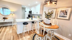 Une cuisine moderne avec des meubles blancs, un îlot central et un coin repas comprenant une table en bois et des chaises blanches.