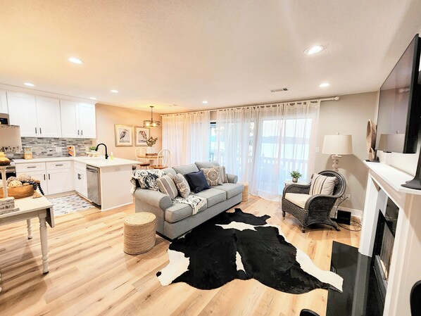 A modern living room with a grey sofa, a black and white cowhide rug, and a dining area with a white table and chairs.