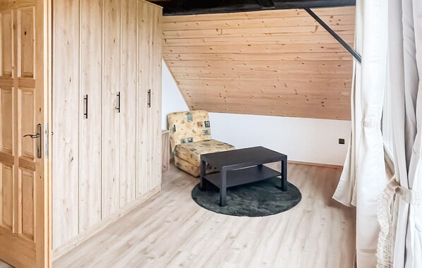 A room with wooden walls, a lofted sleeping area with a patterned chair, and a small table.