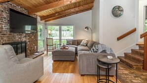 Un salón amplio con chimenea, un ventanal grande, una escalera y un televisor de pantalla plana montado en la pared.