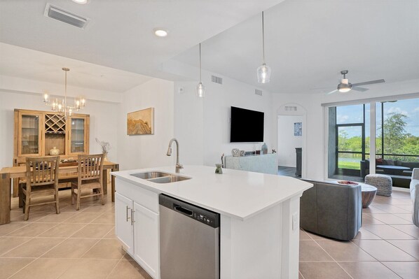 A modern kitchen with a central island, a dining area with wooden furniture, and a living room with a large window.
