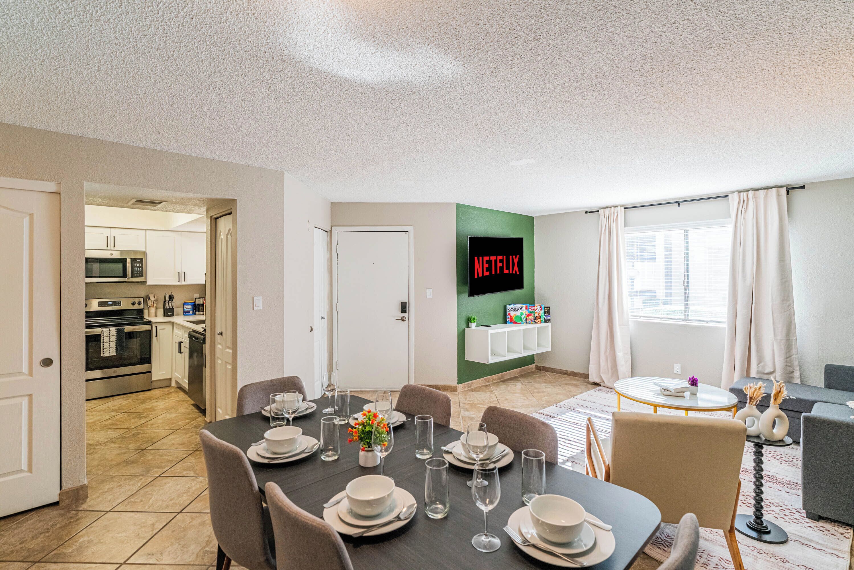 A modern apartment with a dining area, kitchen, living room, and a TV wall.