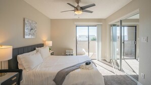 A hotel room with a bed, a ceiling fan, a large window, and a view of the outdoors.