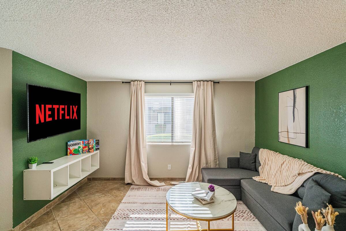 A living room with a flat-screen TV, a sofa, a coffee table, and a window with curtains.