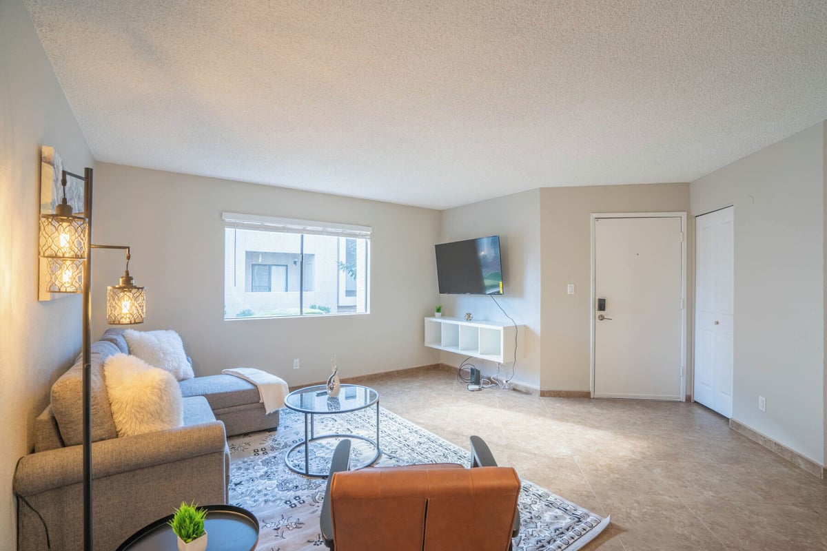 A spacious living room with a sofa, a coffee table, and a TV mounted on the wall.
