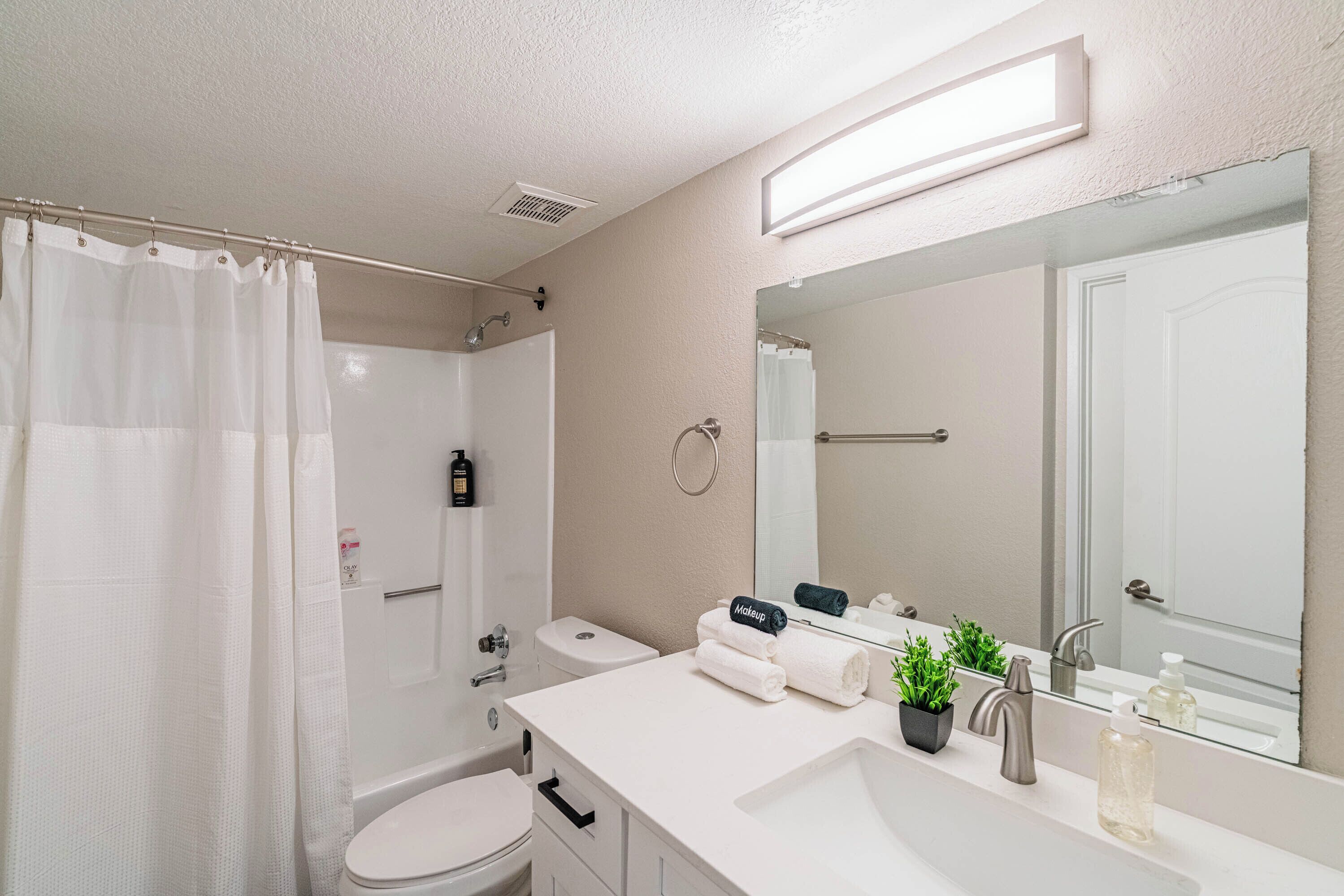 A modern bathroom with a shower, toilet, sink, and a large mirror.