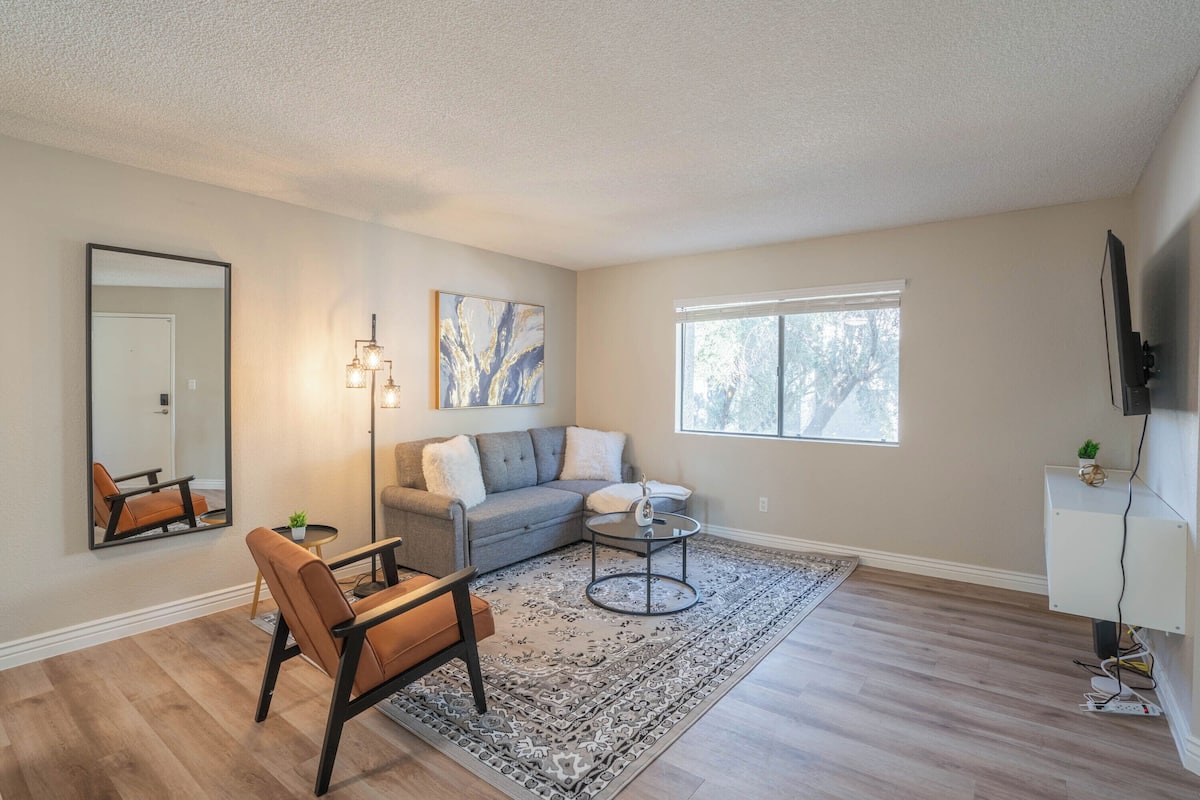 A living room with a grey sofa, a brown armchair, a coffee table, and a patterned rug.
