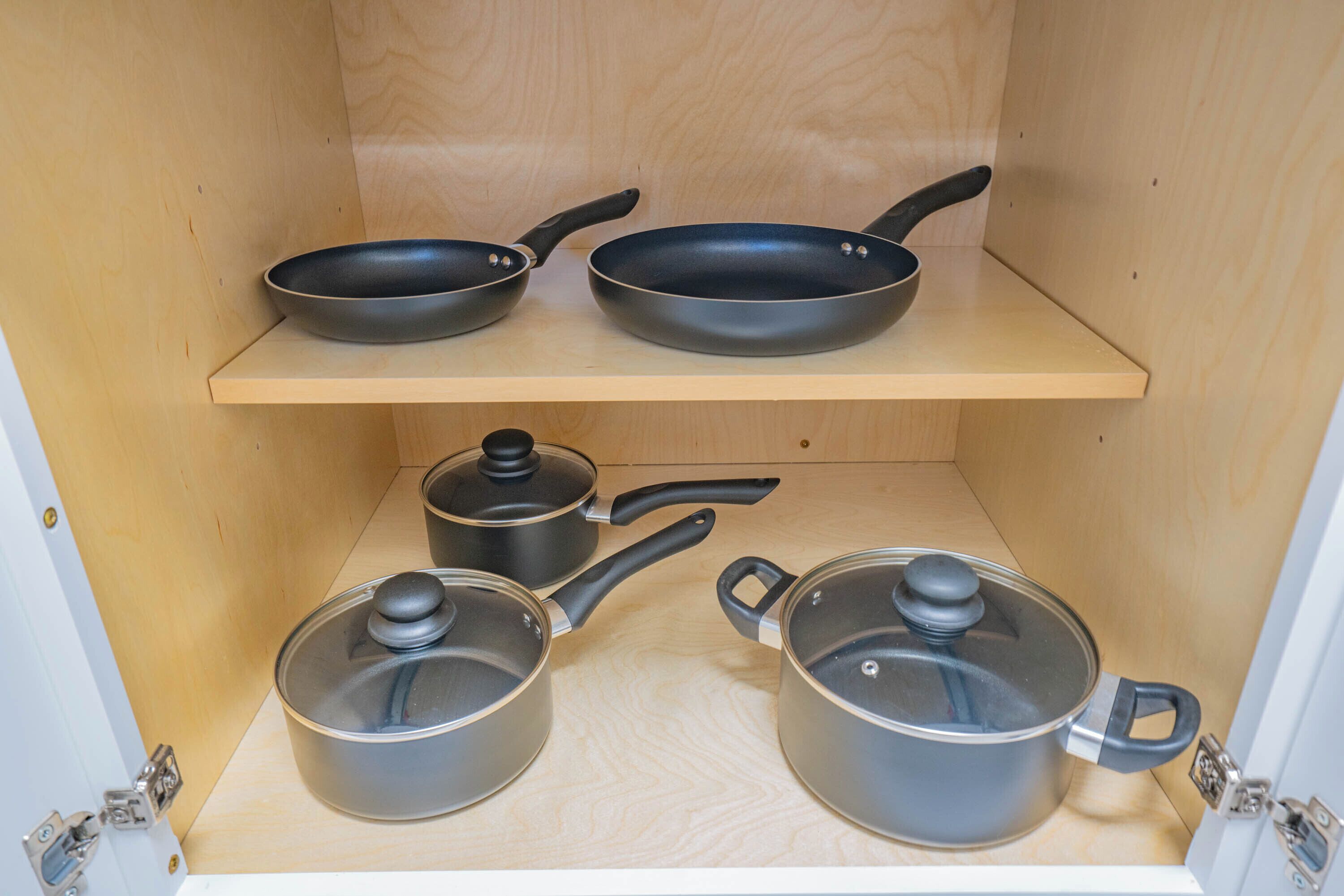 Un armario de cocina con dos sartenes en el estante superior y dos ollas en el inferior.