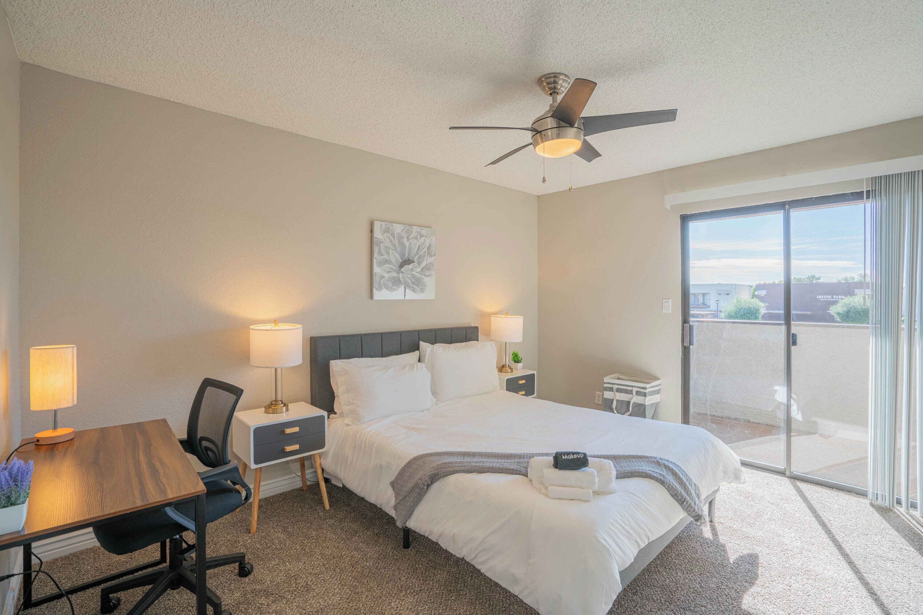 A hotel room with a bed, desk, chair, lamps, and a balcony with a view.