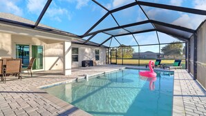Ein heller, überdachter Innenpool mit Blick ins Freie, ein Flamingo-Schwimmpfad und eine überdachte Terrasse mit Stühlen und Tisch.