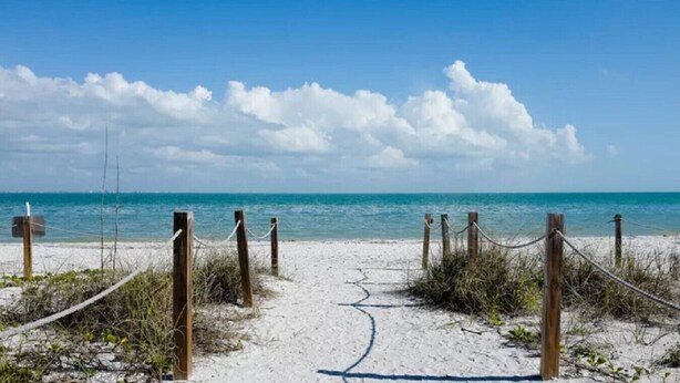 Ein sandiger Strandweg führt zum Meer, mit Holzpfosten und Seilen, die den Eingang kennzeichnen.