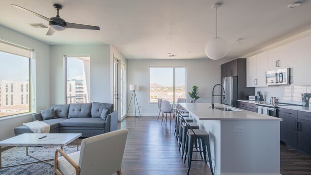 Una sala moderna con un sofá gris, una mesa de centro y un comedor con taburetes de bar.