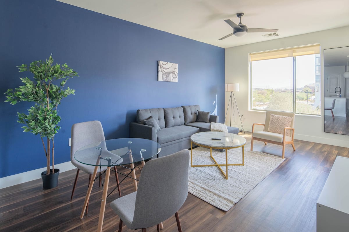 A modern living room with a blue accent wall, a grey sofa, a round coffee table, and a potted plant.