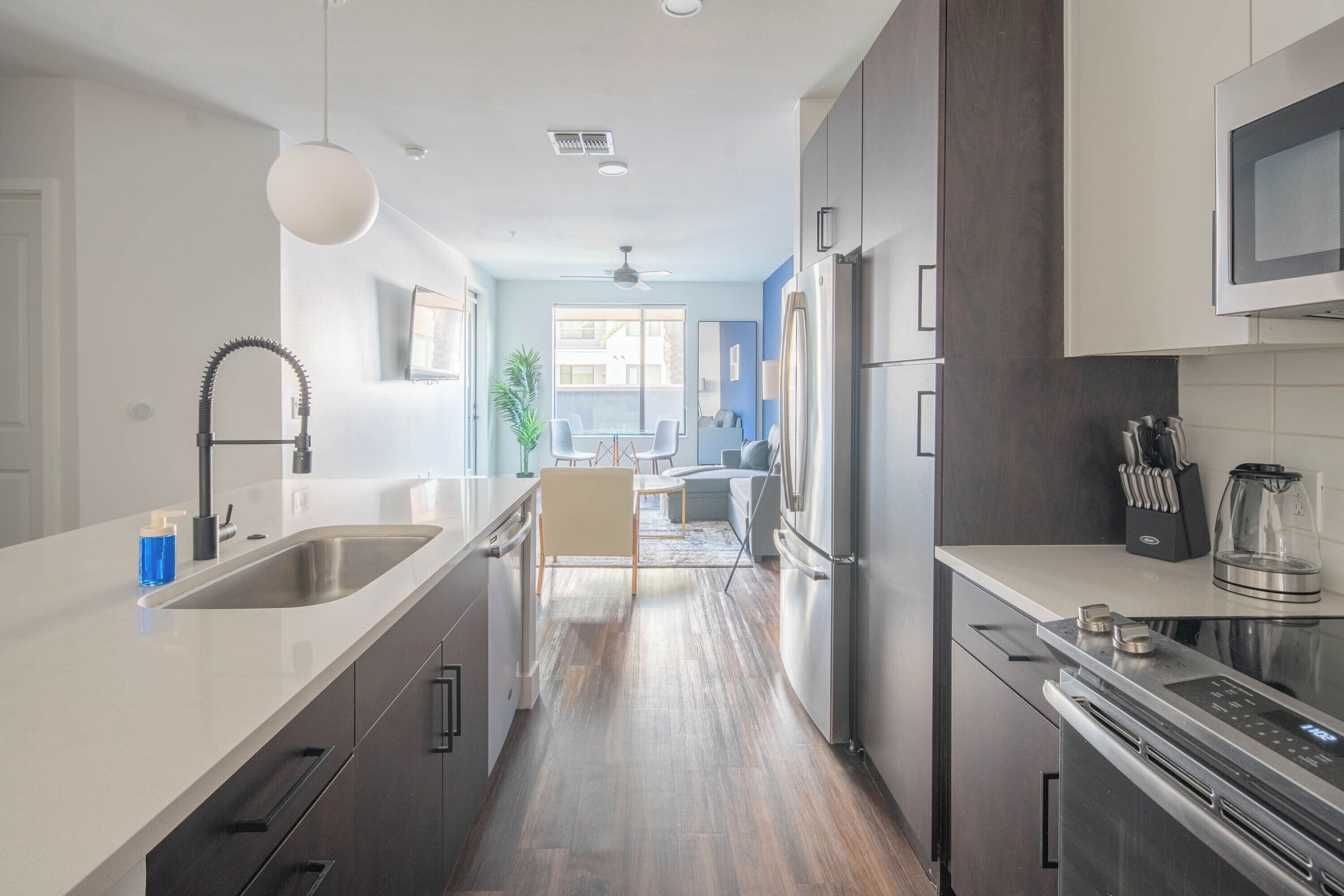 A modern kitchen with stainless steel appliances, a white countertop, and a dining area with a view.
