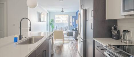 A modern kitchen with stainless steel appliances, a white countertop, and a dining area with a view.