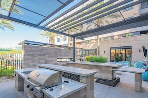 An outdoor patio with a grill, seating area, and a view of the building in the background.