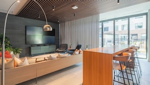 Una cocina moderna con una encimera de madera larga y taburetes, una zona de estar integrada con cojines y un televisor de pantalla plana grande montado en la pared.
