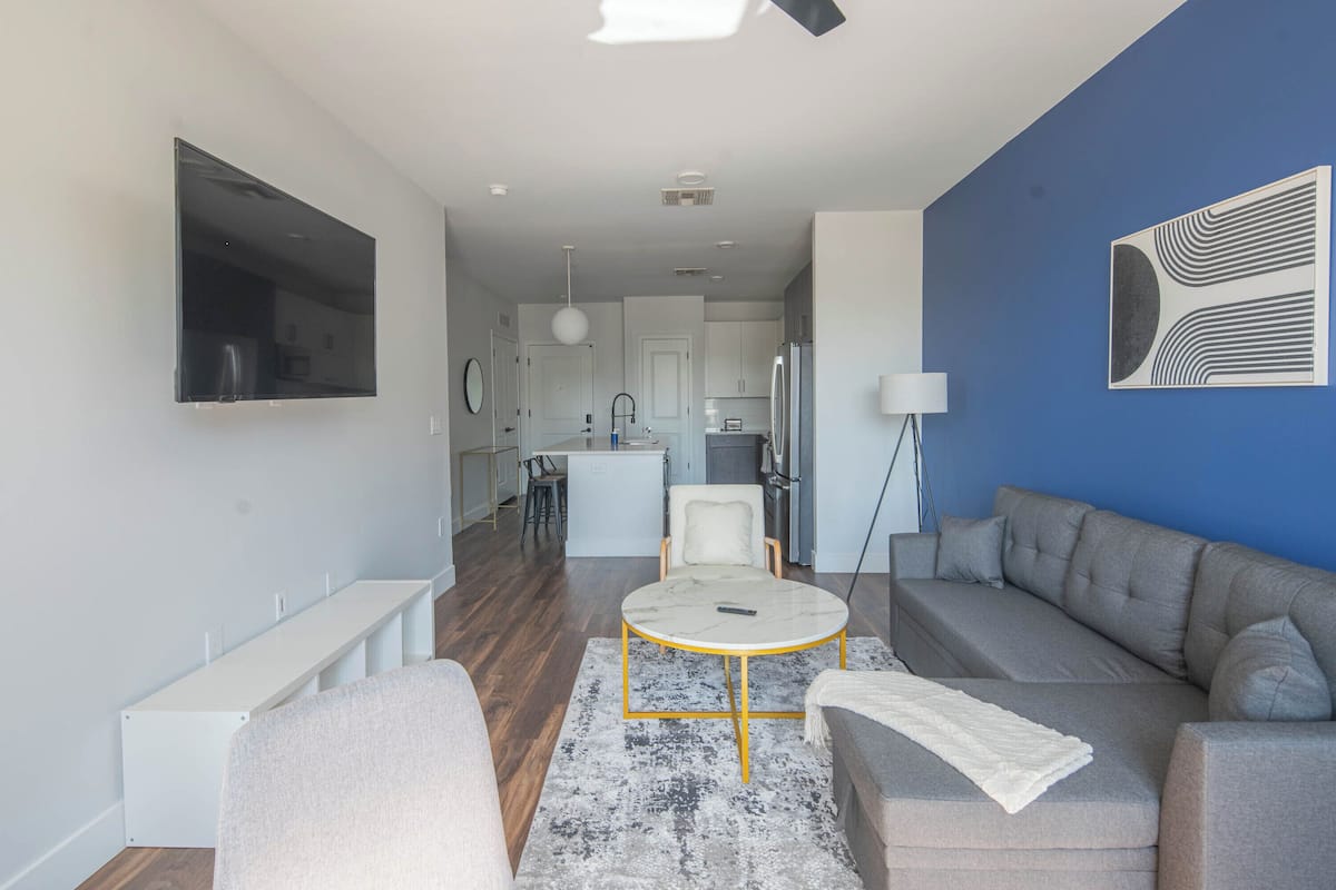 A modern living room with a grey sofa, a round coffee table, and a TV mounted on the wall.