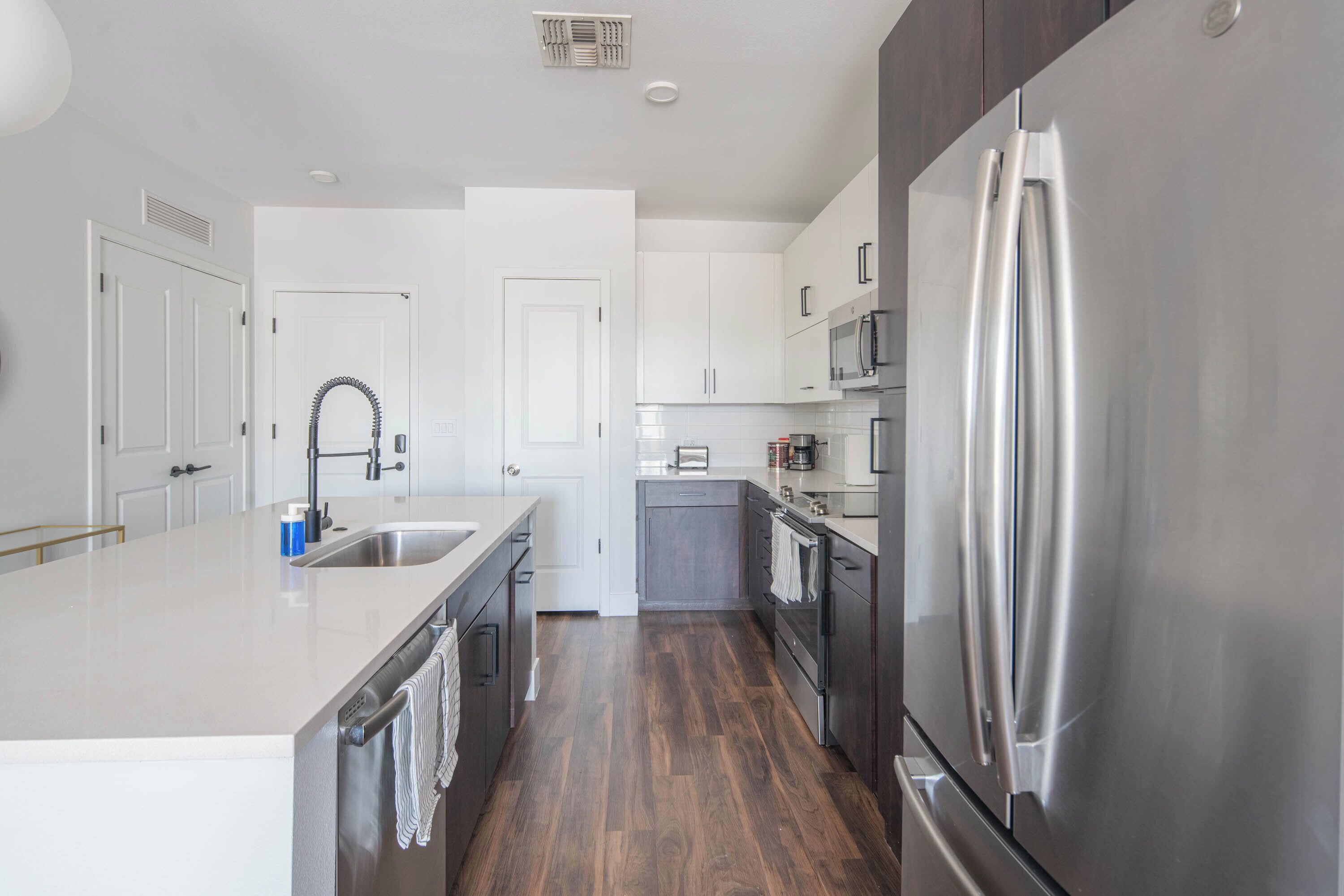 A modern kitchen with stainless steel appliances, white cabinetry, and a wooden floor.