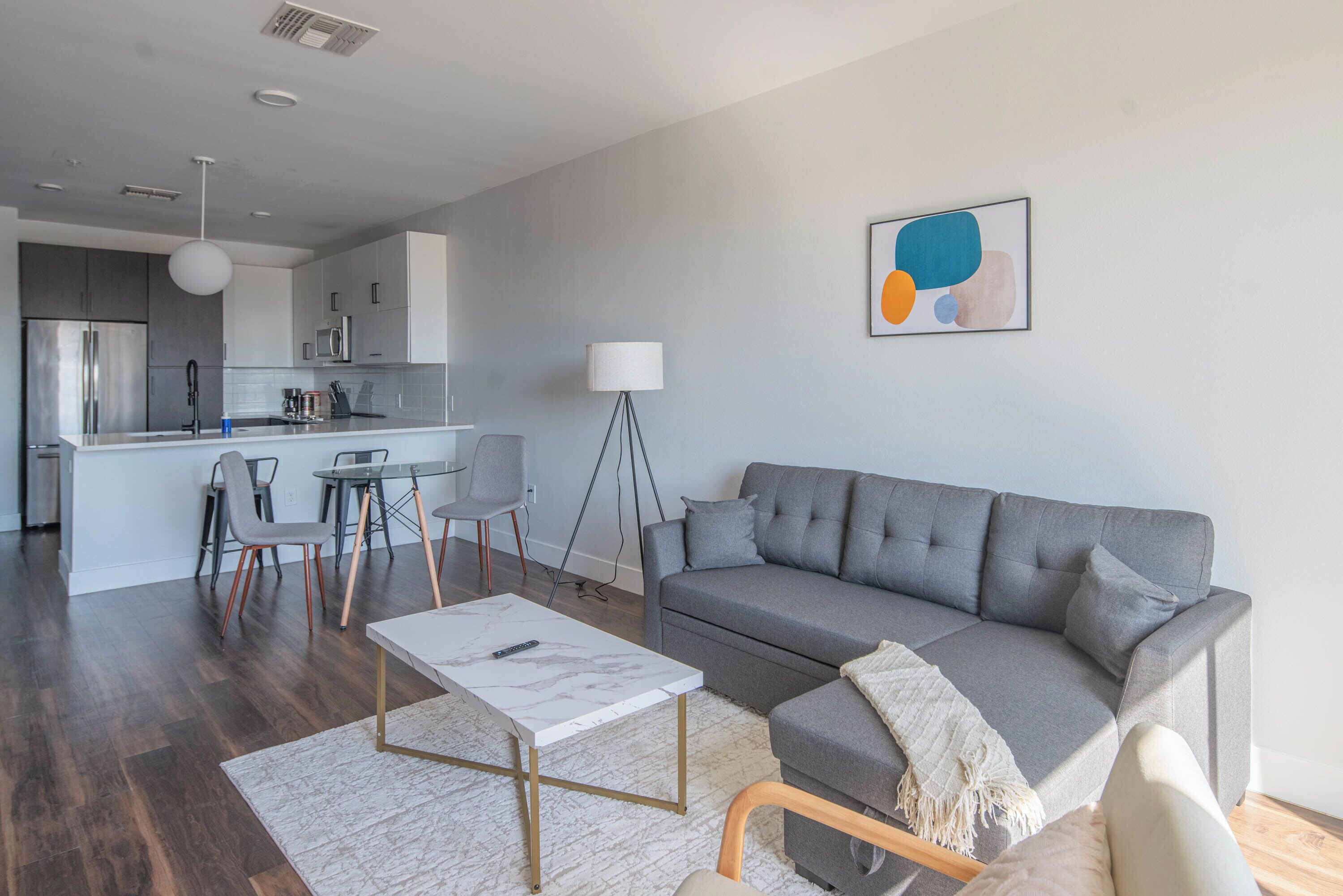 Een moderne woonkamer met een grijze bank, een salontafel en een eethoek met stoelen en een kleine tafel.