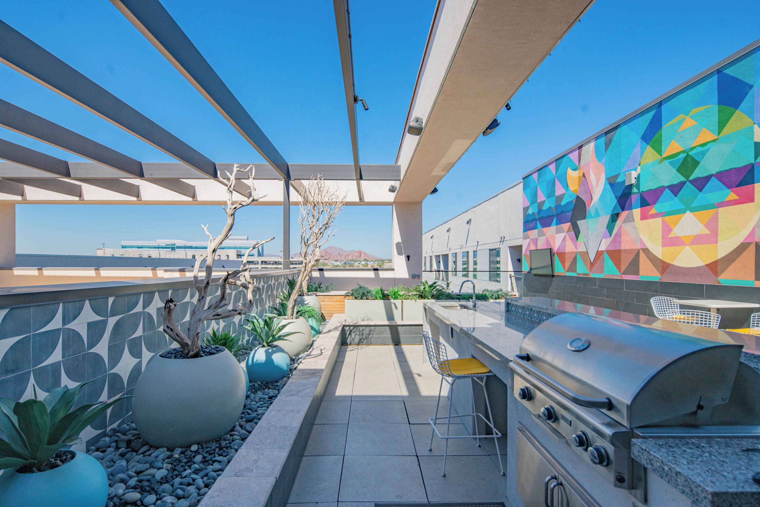 A rooftop patio with a grill, seating, and potted plants.