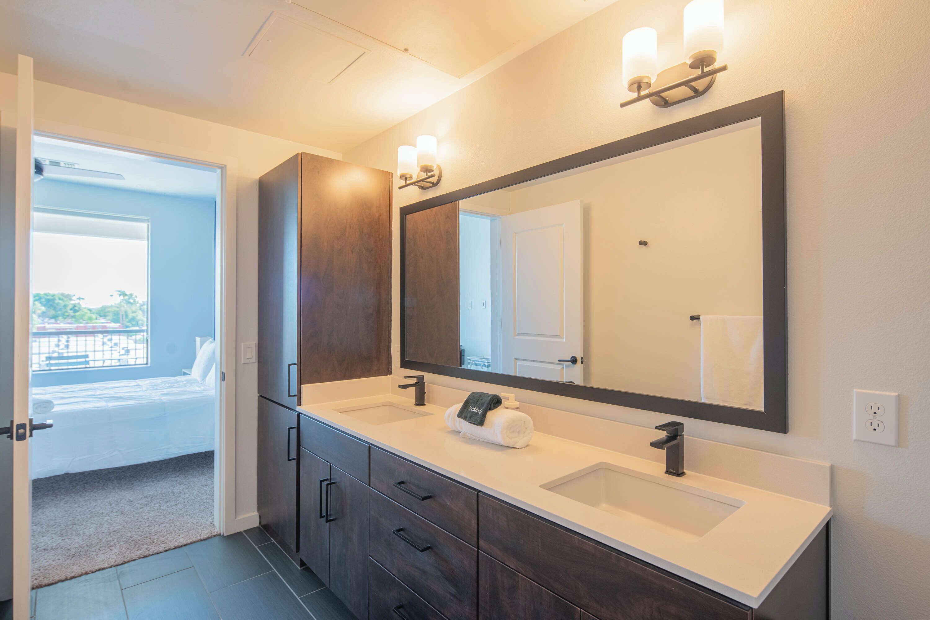 A modern bathroom with two sinks, dark wood cabinets, a large mirror, and a towel rack.
