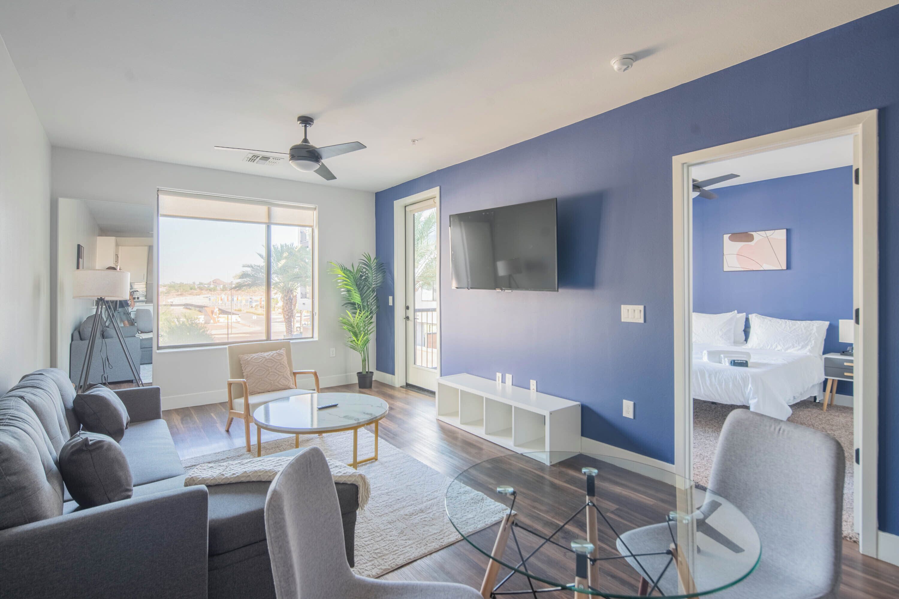 A modern living room with a sofa, chairs, a glass coffee table, and a TV mounted on the wall.