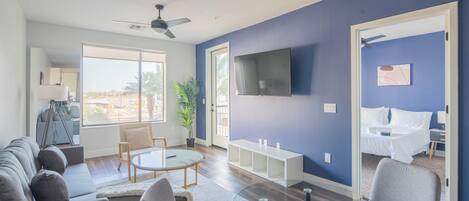 A modern living room with a sofa, chairs, a glass coffee table, and a TV mounted on the wall.